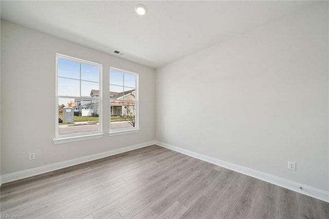 empty room with light wood-type flooring, visible vents, and baseboards