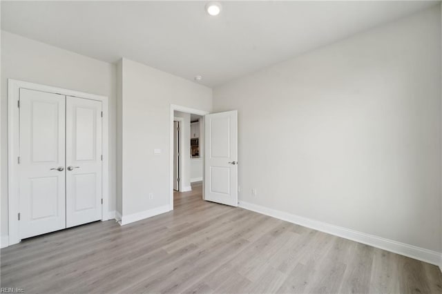 unfurnished bedroom featuring light wood-type flooring, a closet, and baseboards