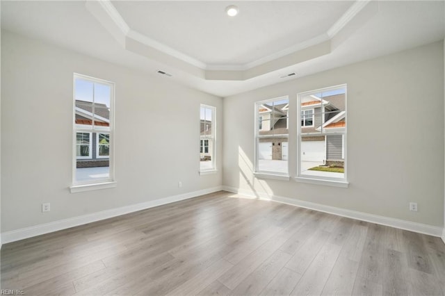 empty room with ornamental molding, a tray ceiling, wood finished floors, and baseboards