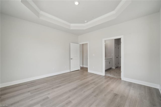 unfurnished bedroom featuring light wood-type flooring, baseboards, a raised ceiling, and ornamental molding