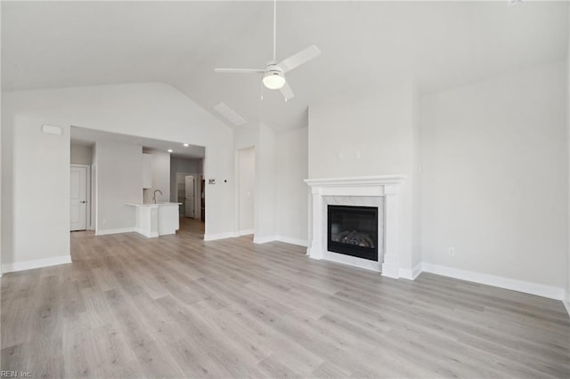 unfurnished living room featuring light wood finished floors, a premium fireplace, ceiling fan, a sink, and baseboards