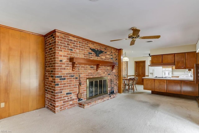 unfurnished living room with a ceiling fan, a brick fireplace, light carpet, and wooden walls