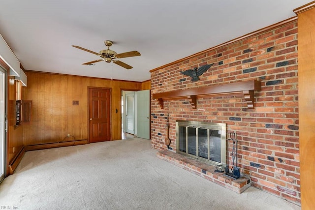 unfurnished living room featuring ceiling fan, wooden walls, carpet floors, a brick fireplace, and crown molding