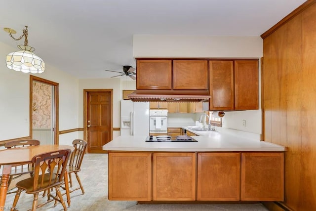 kitchen featuring light countertops, brown cabinetry, a sink, white appliances, and a peninsula