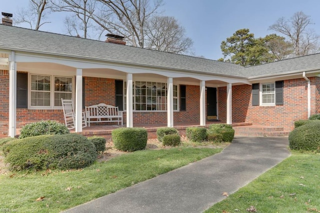 view of front of home featuring covered porch, brick siding, and a chimney