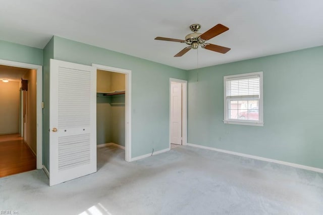 unfurnished bedroom featuring carpet flooring, a ceiling fan, baseboards, a closet, and a walk in closet