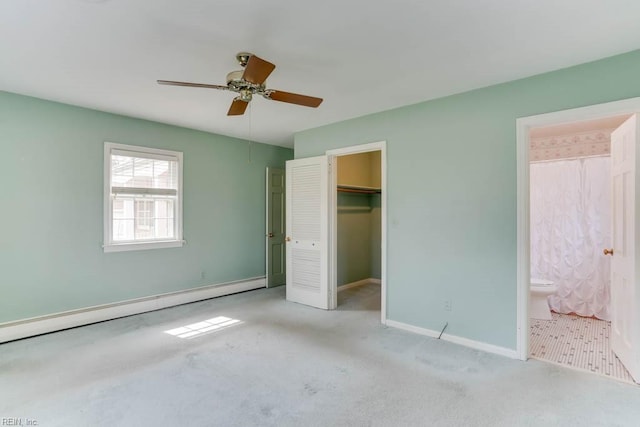 unfurnished bedroom with ensuite bathroom, a baseboard heating unit, carpet floors, baseboards, and a walk in closet