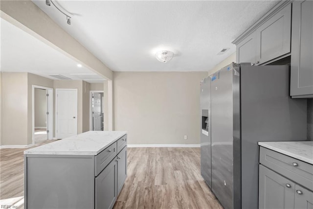 kitchen featuring light wood finished floors, stainless steel fridge, a kitchen island, and gray cabinets