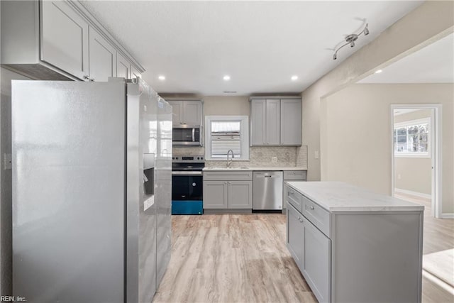 kitchen featuring stainless steel appliances, gray cabinets, decorative backsplash, a sink, and light wood-type flooring