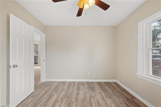 spare room with light wood finished floors, a ceiling fan, and baseboards