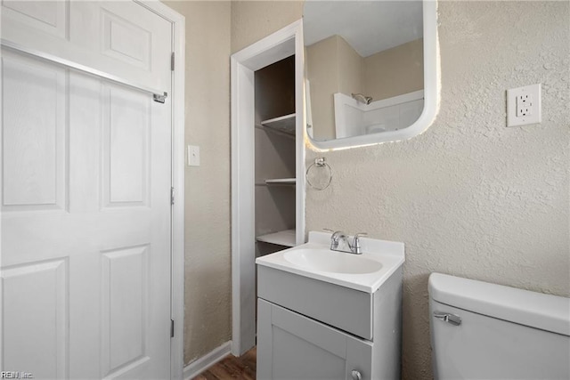 bathroom featuring a textured wall, vanity, and toilet