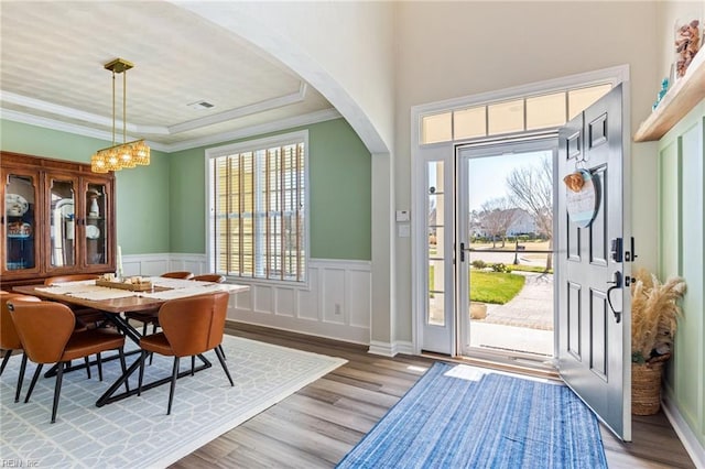 entryway with a chandelier, ornamental molding, a wainscoted wall, and light wood-style flooring