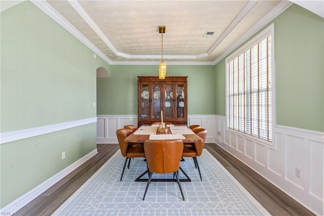 dining room featuring arched walkways, a wainscoted wall, visible vents, ornamental molding, and wood finished floors