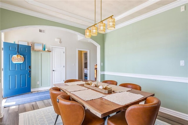 dining area with ornamental molding, arched walkways, visible vents, and wood finished floors