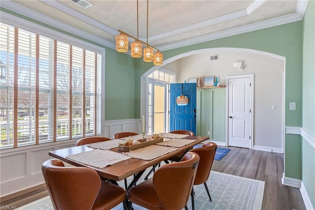 dining space with arched walkways, a wainscoted wall, visible vents, ornamental molding, and wood finished floors