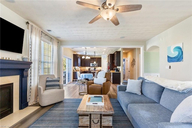 living area featuring ceiling fan with notable chandelier, a fireplace, wood finished floors, and visible vents