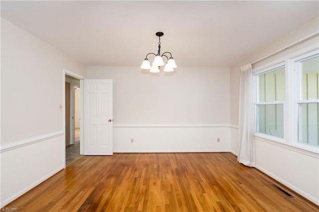 empty room featuring visible vents, wood finished floors, baseboards, and a chandelier