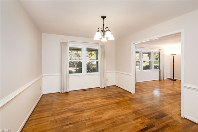 spare room with a notable chandelier, baseboards, and wood finished floors