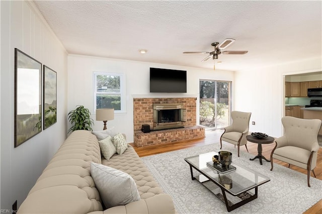 living area featuring ceiling fan, a textured ceiling, a brick fireplace, and wood finished floors