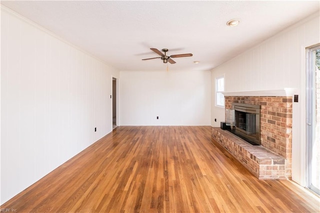 unfurnished living room with light wood-type flooring, a brick fireplace, and a ceiling fan