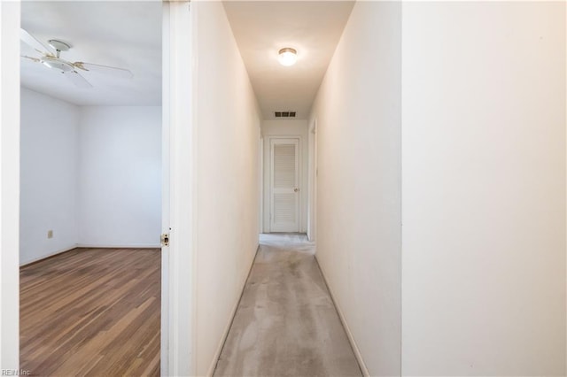 hallway with baseboards, visible vents, and light wood finished floors