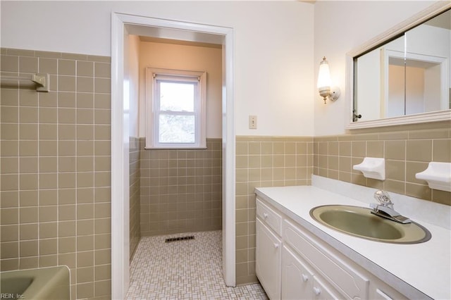 bathroom with visible vents, tile walls, wainscoting, walk in shower, and vanity