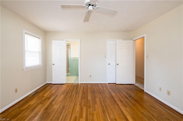 unfurnished bedroom with visible vents, ceiling fan, baseboards, wood finished floors, and ensuite bath