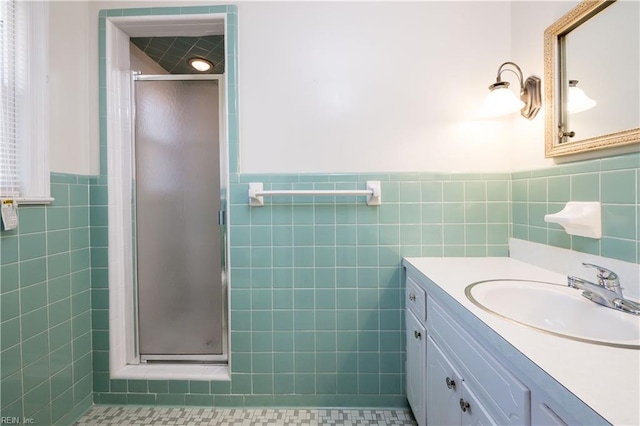 full bath featuring vanity, tile walls, a stall shower, and wainscoting