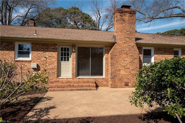 rear view of house featuring a patio, brick siding, roof with shingles, and a chimney