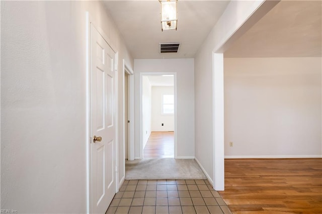 hall with light tile patterned flooring, visible vents, light colored carpet, and baseboards