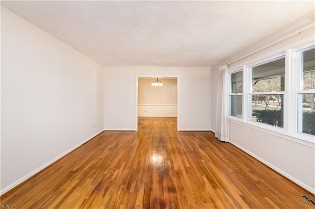 empty room with visible vents, baseboards, an inviting chandelier, and wood finished floors