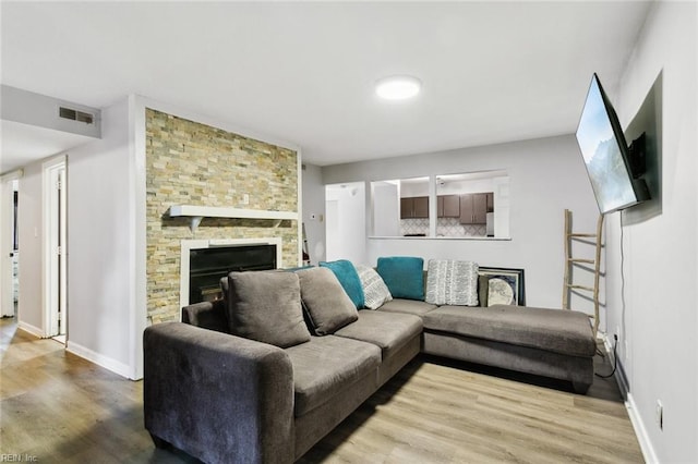 living area featuring baseboards, visible vents, wood finished floors, and a stone fireplace