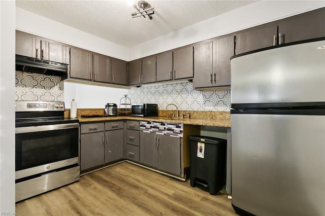 kitchen with tasteful backsplash, light wood-style flooring, appliances with stainless steel finishes, a textured ceiling, and under cabinet range hood