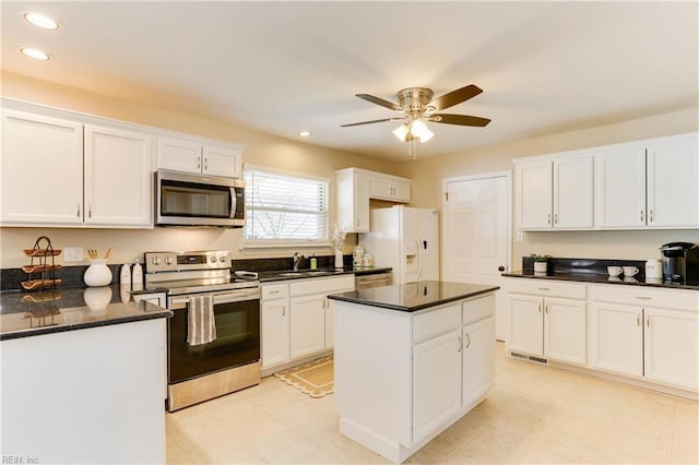 kitchen with dark countertops, a center island, stainless steel appliances, white cabinetry, and a sink