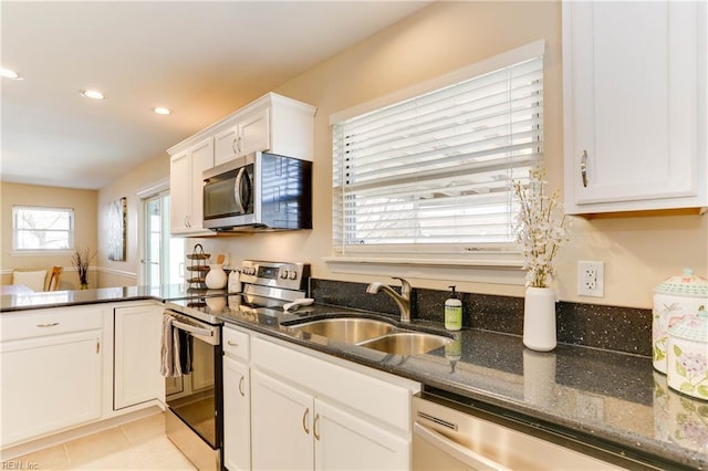 kitchen with light tile patterned flooring, stainless steel appliances, a peninsula, a sink, and white cabinetry