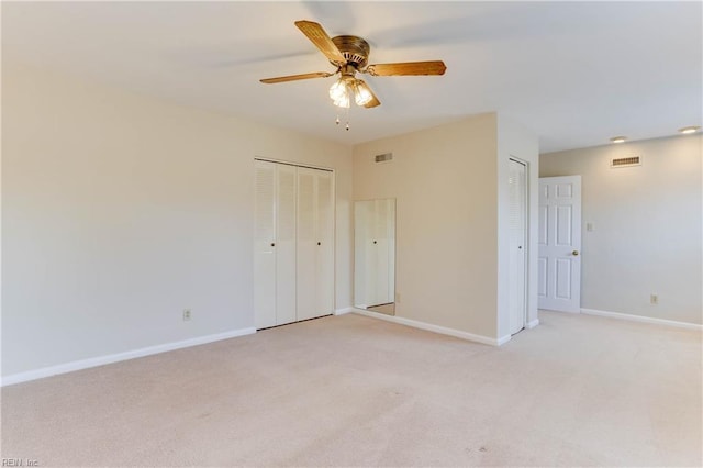 unfurnished bedroom featuring multiple closets, visible vents, light carpet, and baseboards