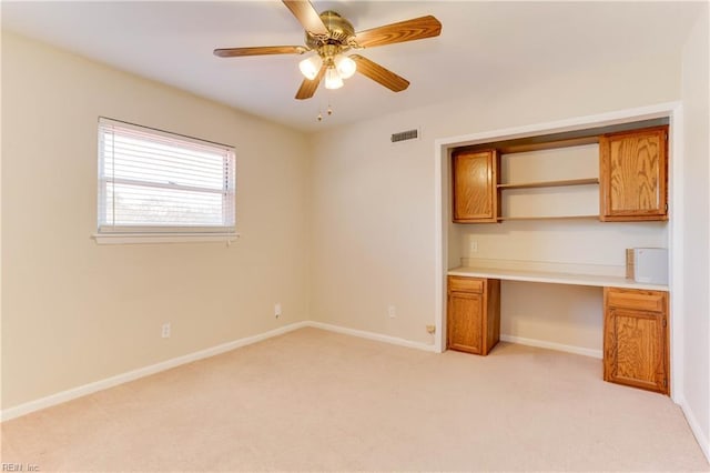 unfurnished office featuring built in desk, visible vents, a ceiling fan, light carpet, and baseboards