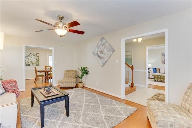 living area featuring light wood-style floors, stairway, baseboards, and a ceiling fan