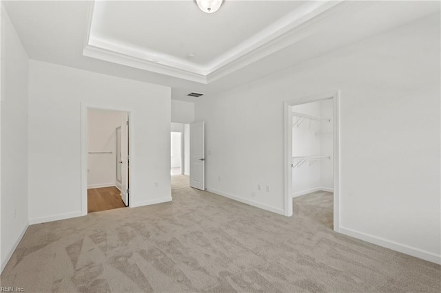 unfurnished bedroom featuring visible vents, baseboards, carpet, a tray ceiling, and a walk in closet