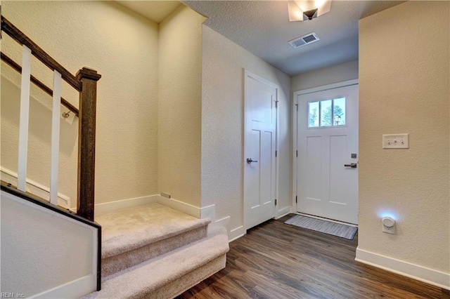 foyer entrance with visible vents, a textured wall, dark wood-type flooring, baseboards, and stairs