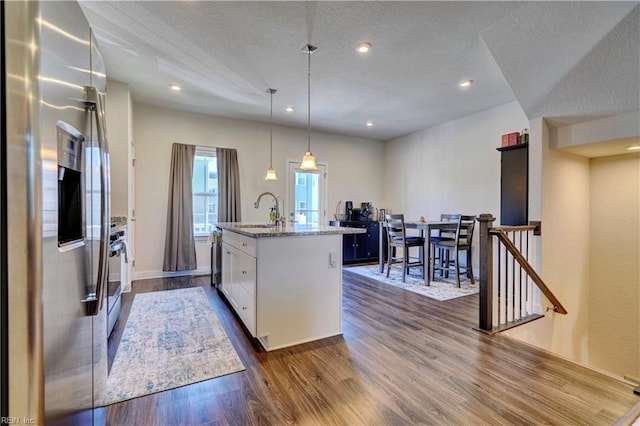 kitchen with a sink, white cabinets, appliances with stainless steel finishes, dark wood-style floors, and a center island with sink