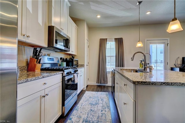 kitchen featuring dark wood-style flooring, a center island with sink, stainless steel appliances, white cabinetry, and a sink