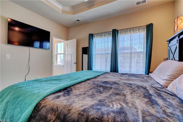 bedroom with ornamental molding, a tray ceiling, and visible vents