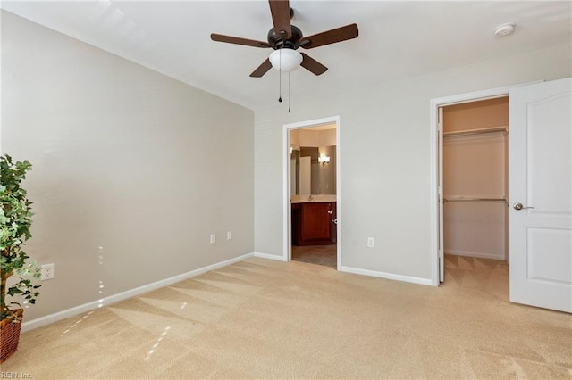 unfurnished bedroom featuring baseboards, light colored carpet, ceiling fan, ensuite bathroom, and a spacious closet