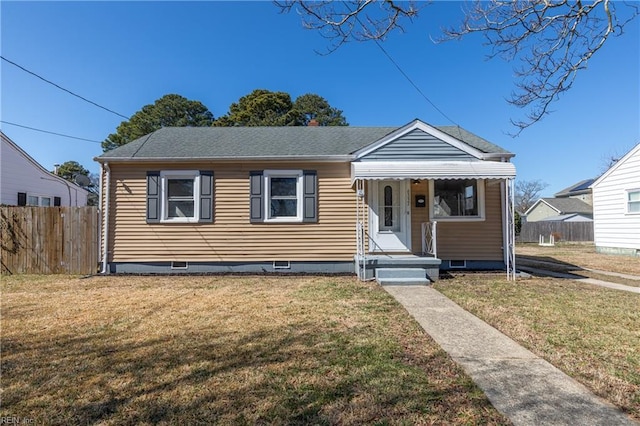 bungalow-style home with a shingled roof, fence, and a front lawn