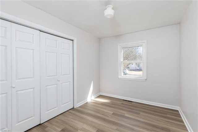 unfurnished bedroom with a closet, wood finished floors, visible vents, and baseboards