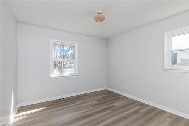 unfurnished room featuring baseboards, plenty of natural light, visible vents, and wood finished floors