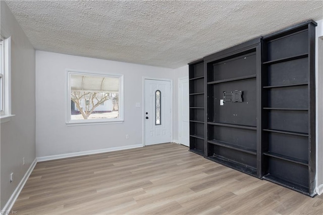 unfurnished room with a textured ceiling, baseboards, and light wood-style floors