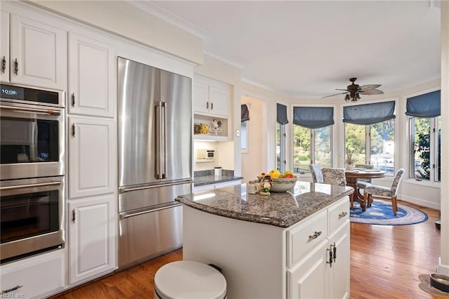 kitchen with stainless steel appliances, a kitchen island, ornamental molding, light wood-type flooring, and dark stone counters