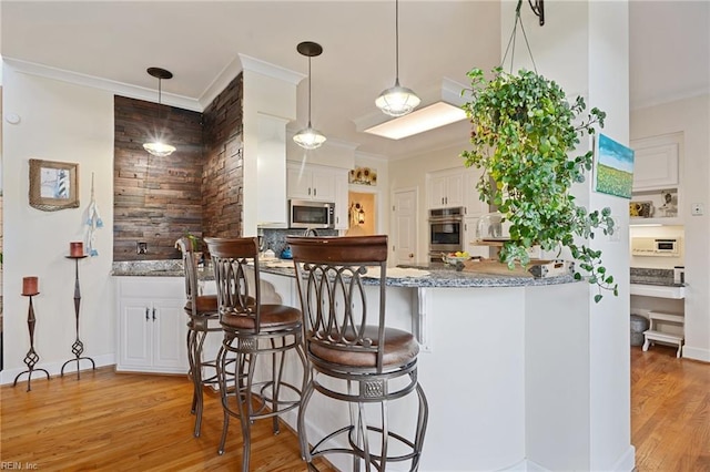 kitchen featuring light wood-style floors, white cabinets, decorative backsplash, stainless steel microwave, and crown molding